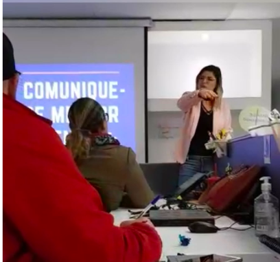 Thaís Guimarães palestrando em sala de reunião, vista a partir da plateia sentada às mesas