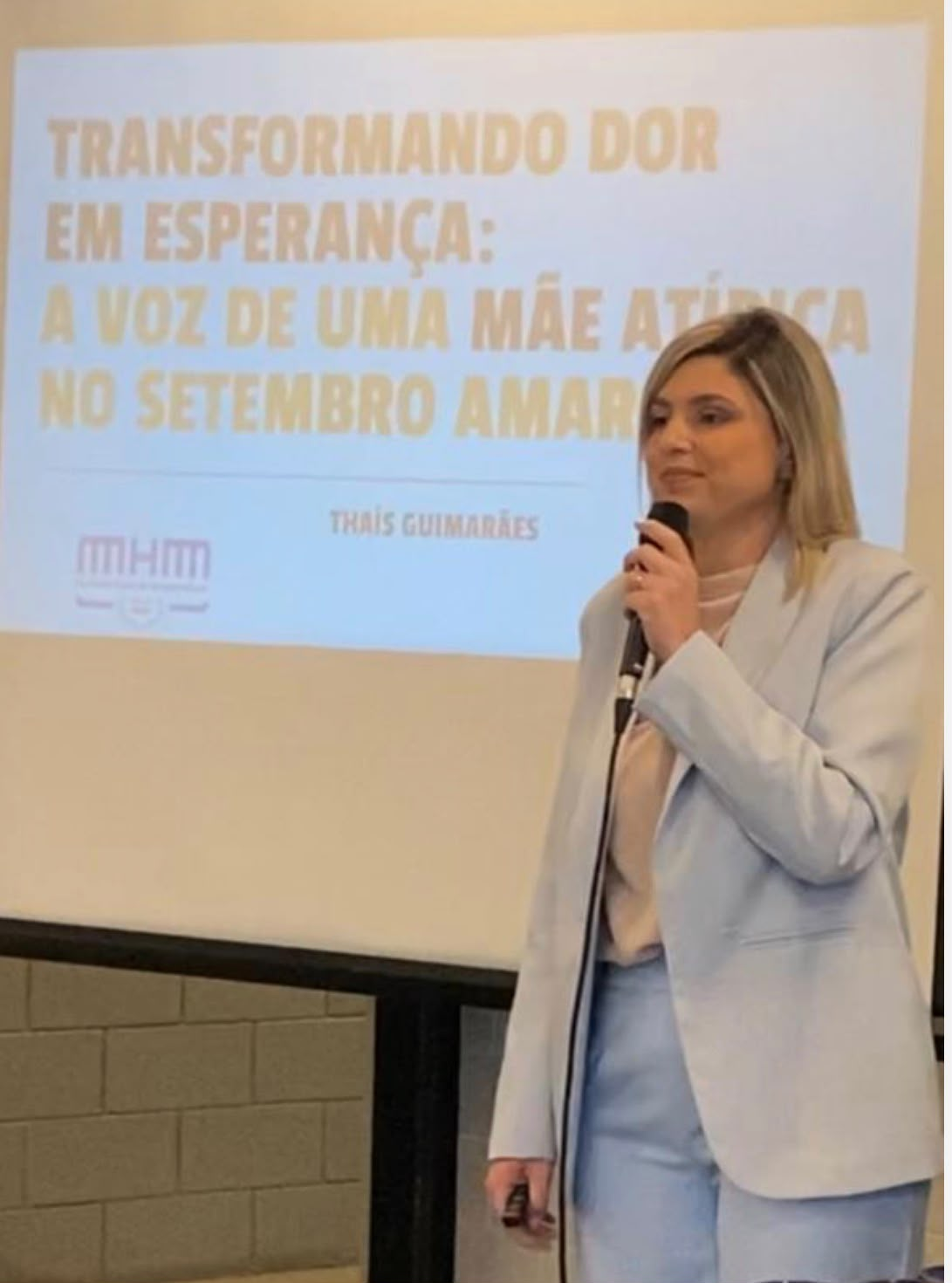 Thaís Guimarães ao microfone durante palestra de Setembro Amarelo, ao lado do slide “Transformando dor em esperança”
