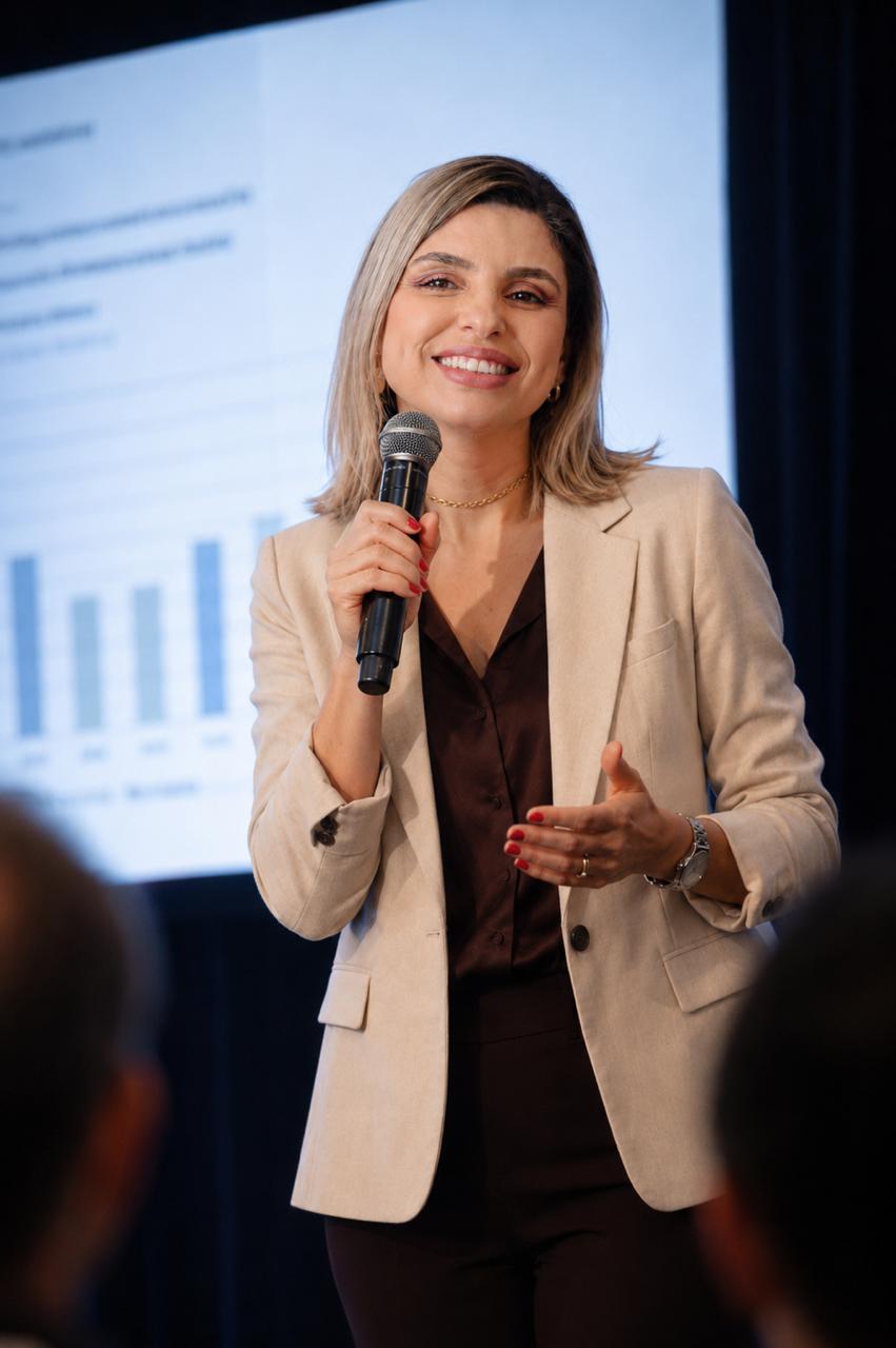 Thaís Guimarães sorrindo ao microfone durante palestra corporativa em auditório