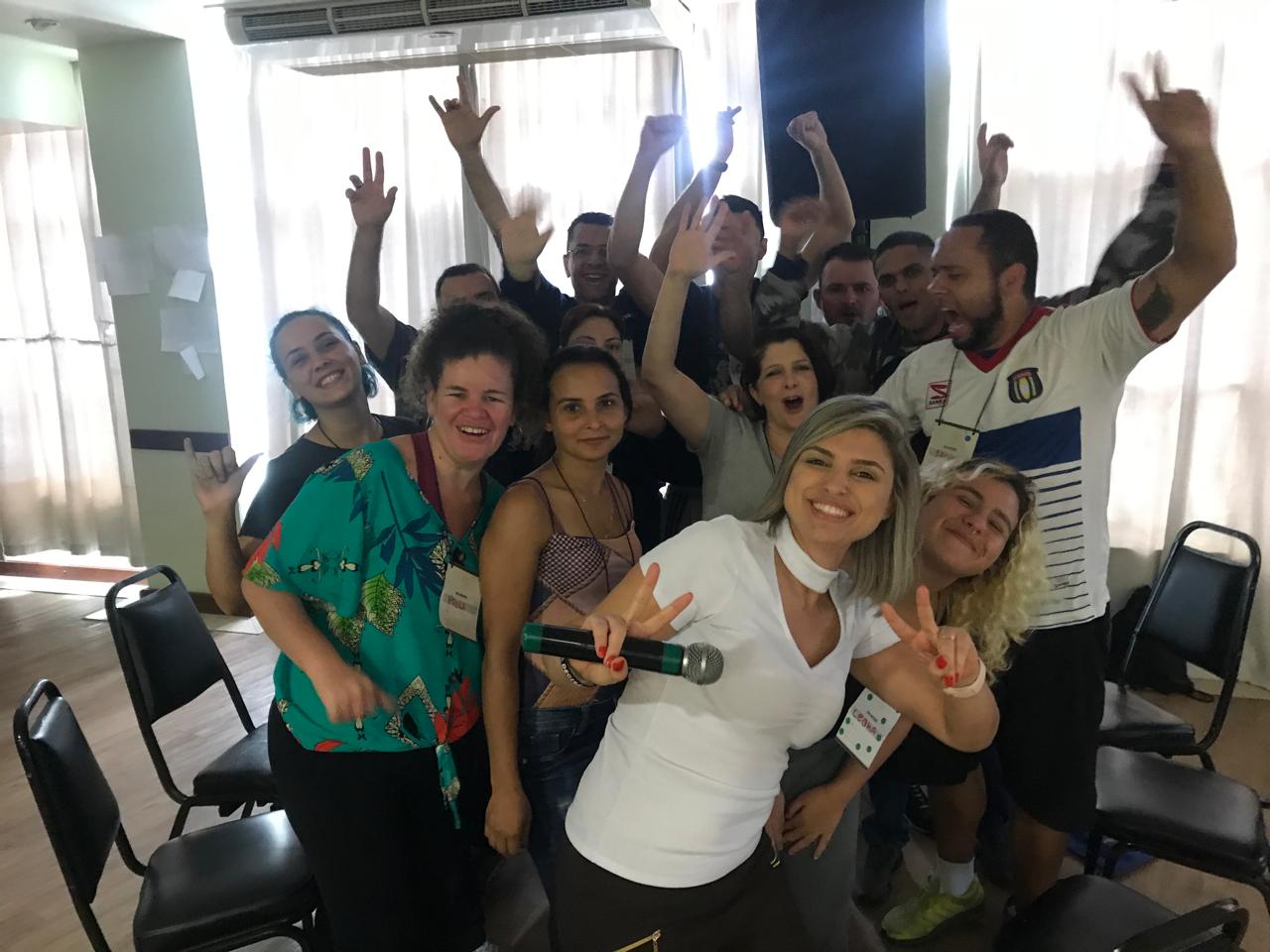 Participantes de uma palestra com os braços erguidos ao lado de Thaís Guimarães após dinâmica em grupo